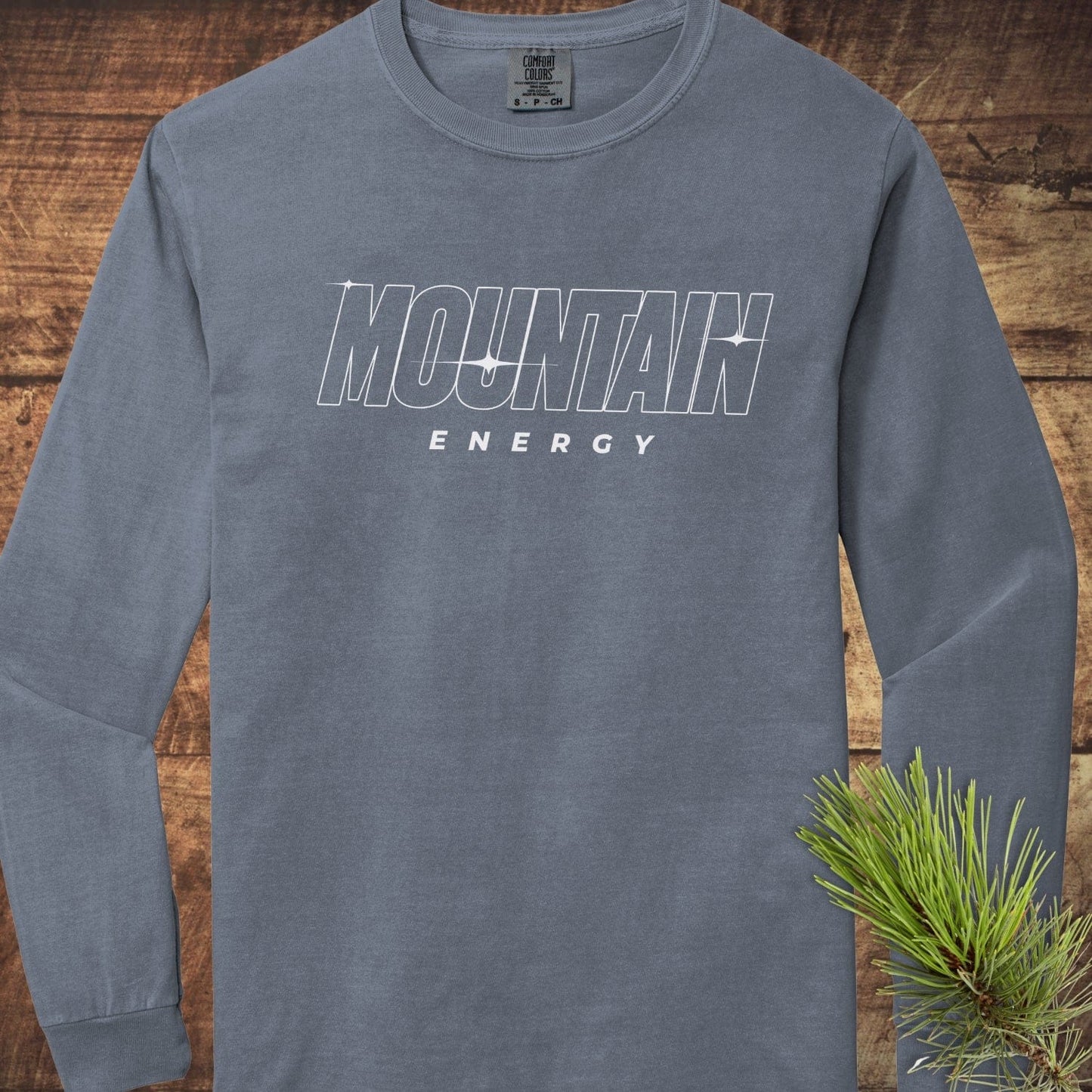Mountain Energy Comfort Colors Longsleeve Tee, slate-blue, with white MOUNTAIN ENERGY graphic on chest, laid flat with pine sprig on sleeve. 