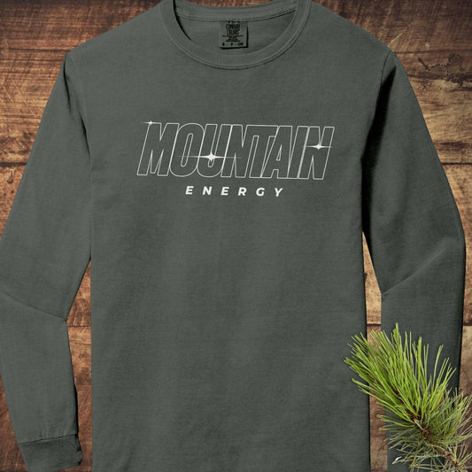 Mountain Energy Comfort Colors Longsleeve Tee, moss-green, with MOUNTAIN ENERGY text. Features 100% ring-spun cotton and relaxed fit, laid flat on wood.