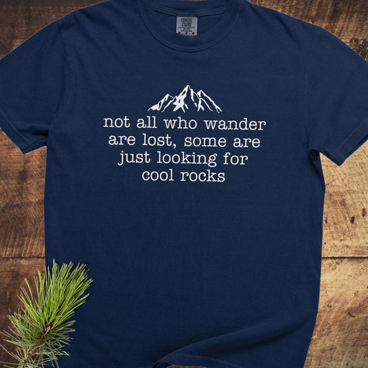 Looking For Cool Rocks Comfort Colors 1717 Tee, navy-blue with mountain graphic and quote, laid on wood. Features durable, soft-washed, 100% ring-spun cotton.