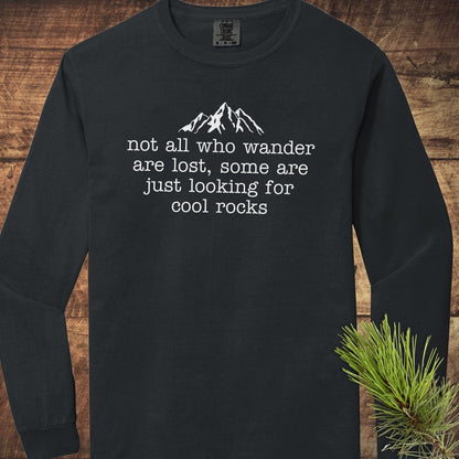 Looking For Cool Rocks Comfort Colors Long-Sleeve Tee features a mountain design and playful quote, laid out on a wooden surface with pine sprig.