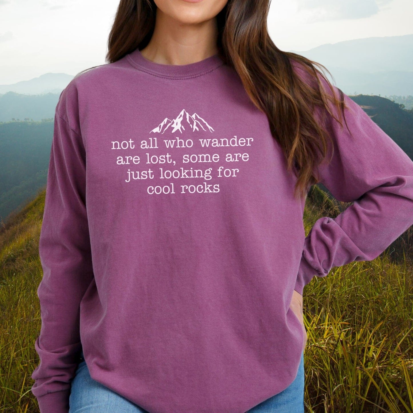Person on hillside wearing Looking For Cool Rocks Comfort Colors Long-Sleeve Tee with mountain graphic, showcasing relaxed fit and soft garment-dyed cotton.
