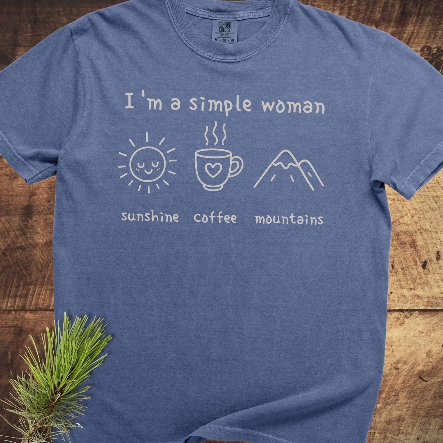 I'm A Simple Woman Comfort Colors 1717 Tee on wood, featuring sunshine, coffee, and mountains icons, emphasizing a casual, relaxed fit.