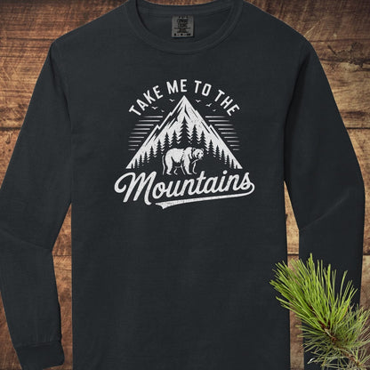 Copy of Mountain Energy Comfort Colors Long-Sleeve Tee featuring a vintage mountain graphic with pine trees and a bear, laid on a wooden surface with a pine needle sprig.