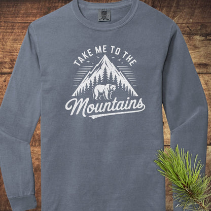 Copy of Mountain Energy Comfort Colors Long-Sleeve Tee featuring a mountain graphic, pine trees, bear silhouette, and “Take Me to the Mountains” slogan on rustic wood background.