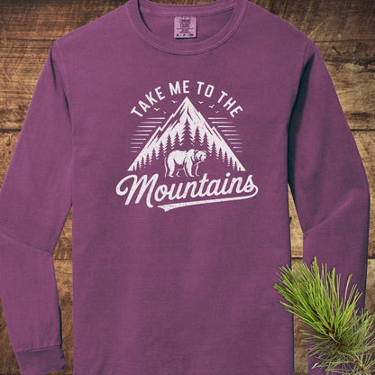 Copy of Mountain Energy Comfort Colors Long-Sleeve Tee featuring a distressed mountain graphic with trees and bear. Laid on wood, adorned with pine needles for ambiance.