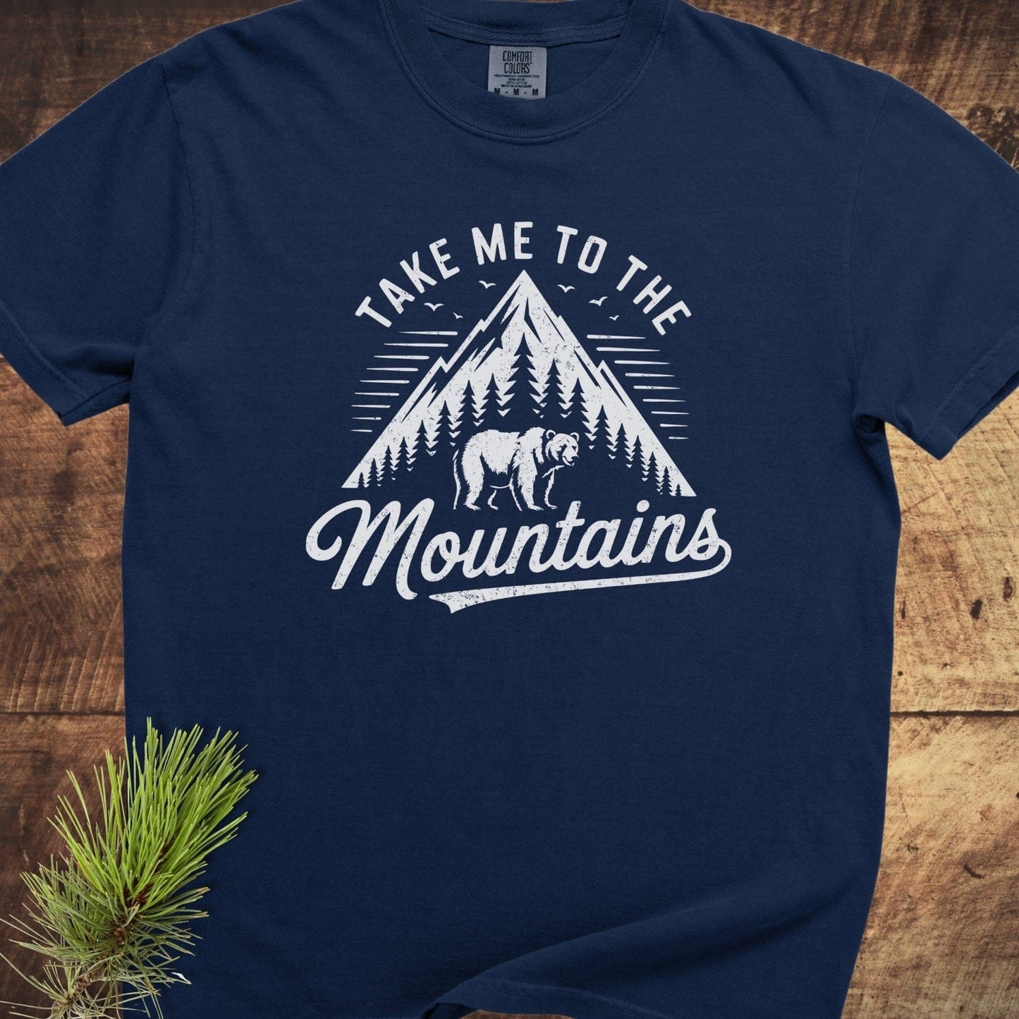 Take Me To The Mountains Comfort Colors 1717 Tee features a mountain graphic with birds and bear, soft-washed 100% cotton, relaxed fit, durable stitching.