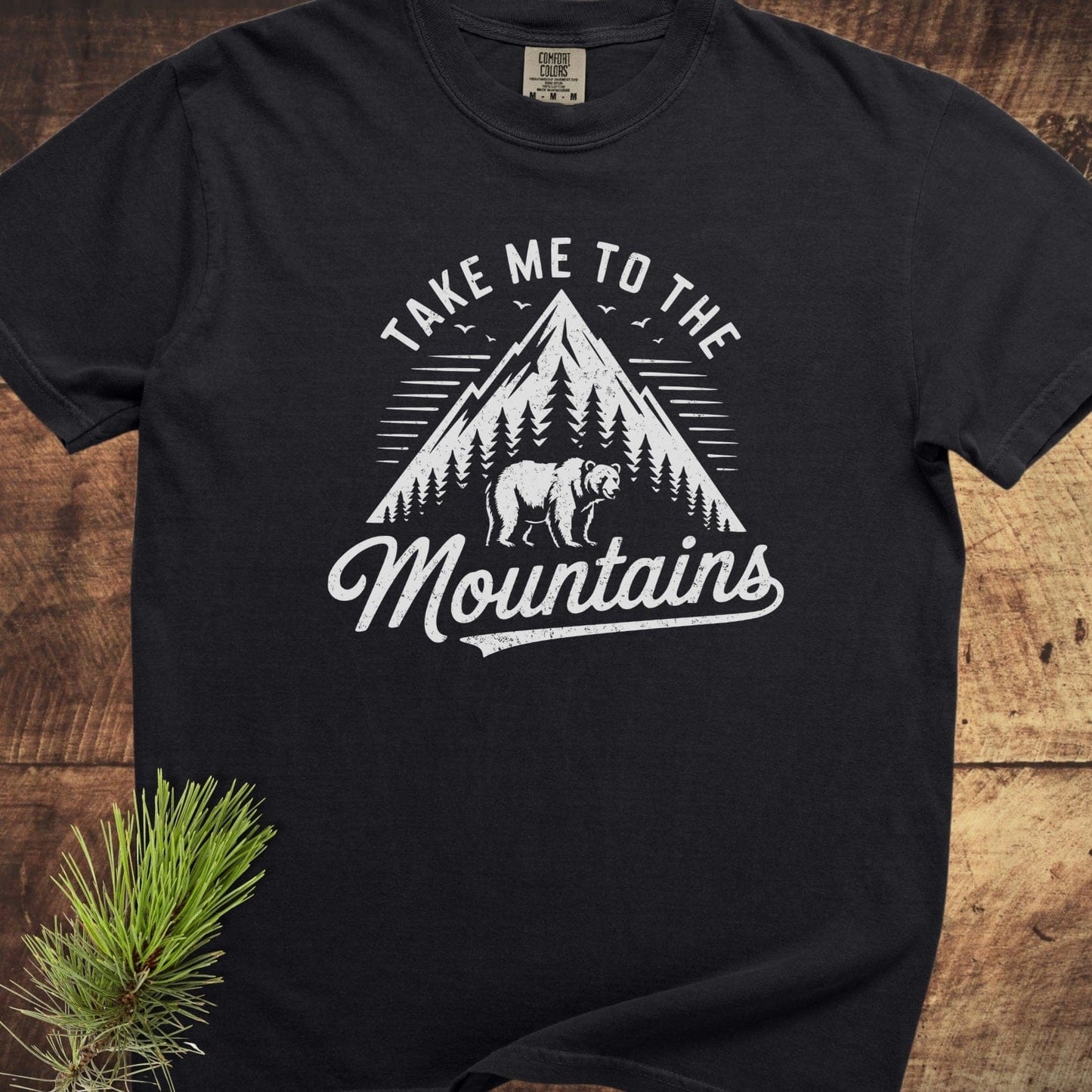 Take Me To The Mountains Comfort Colors 1717 Tee displays a mountain graphic, pine trees, and a bear on a black, soft-washed, garment-dyed t-shirt.