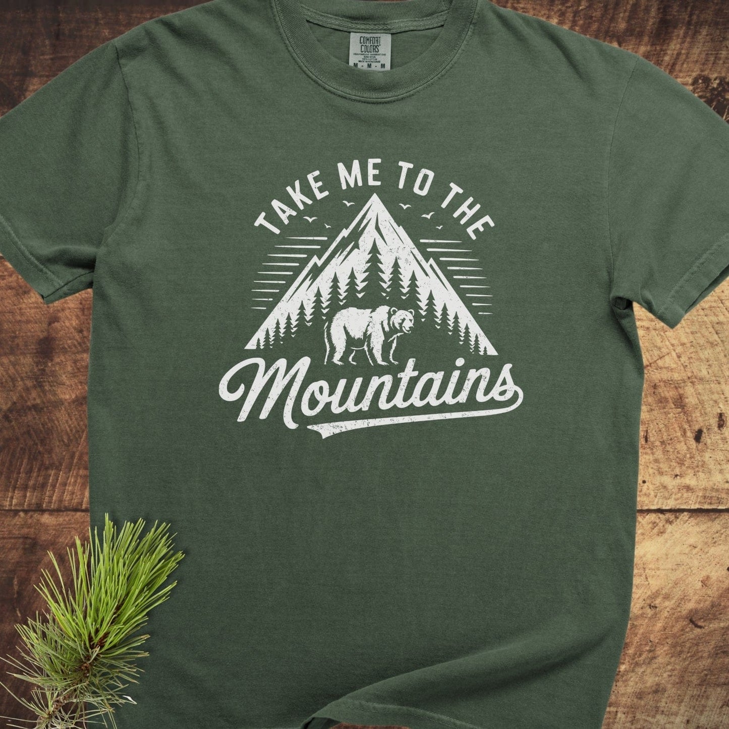 Take Me To The Mountains Comfort Colors 1717 Tee with mountain and bear graphic, laid flat, showcasing its forest-green, relaxed fit and durable, soft-washed cotton fabric.