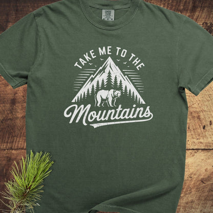 Take Me To The Mountains Comfort Colors 1717 Tee with mountain and bear graphic, laid flat, showcasing its forest-green, relaxed fit and durable, soft-washed cotton fabric.