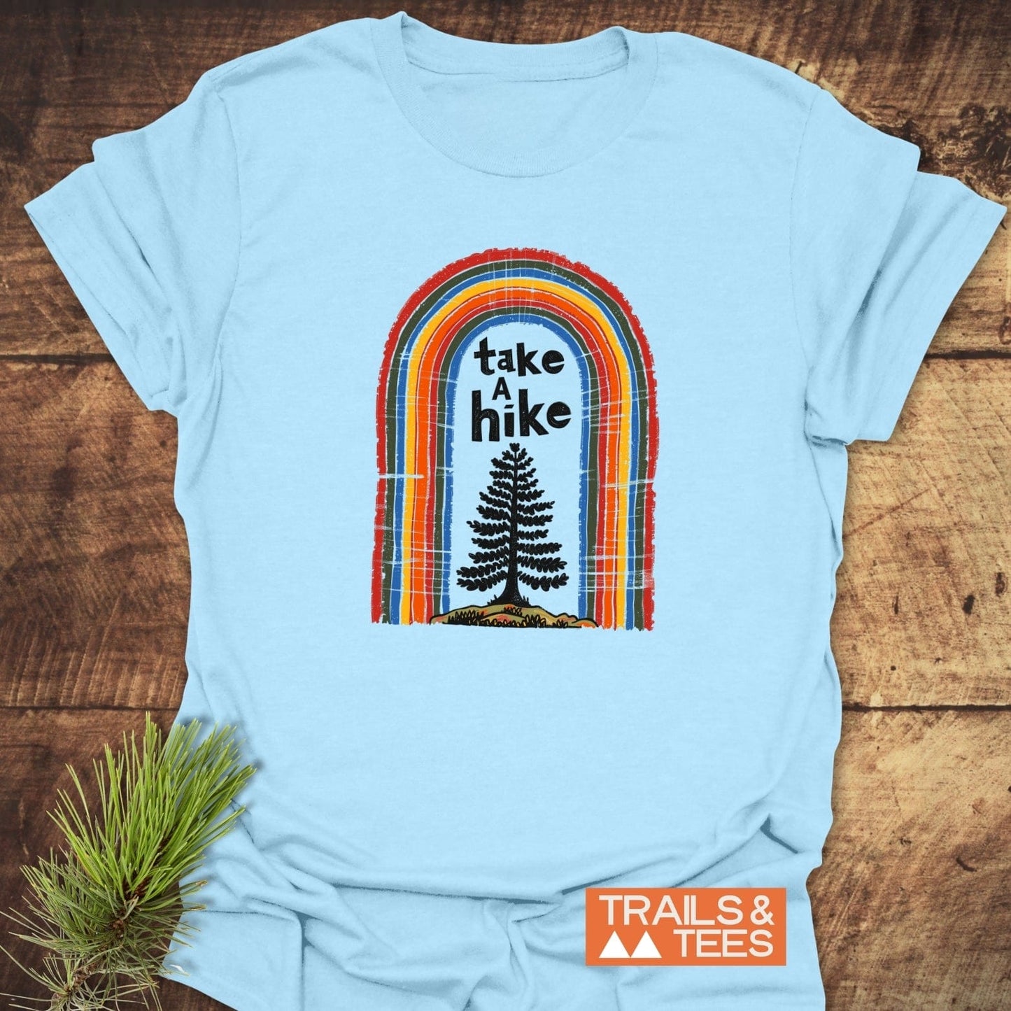 Take A Hike Rainbow T-Shirt featuring a retro graphic with a rainbow arch and pine tree silhouette, crafted from soft, lightweight cotton for outdoor enthusiasts.