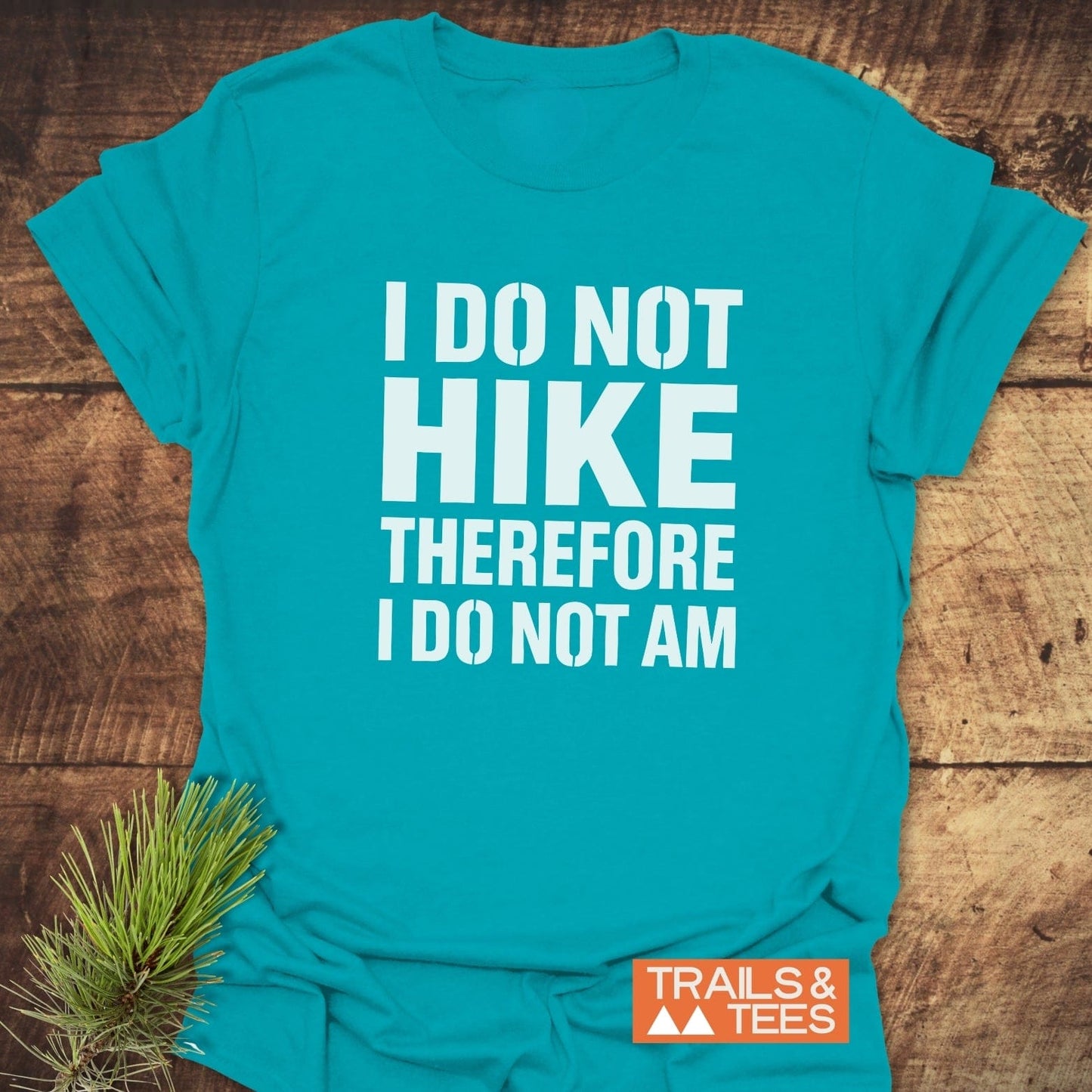 Teal I Do Not Hike T-shirt on wood surface, featuring white slogan, TRAILS & TEES logo, crafted for comfort and durability, ideal for outdoor enthusiasts.
