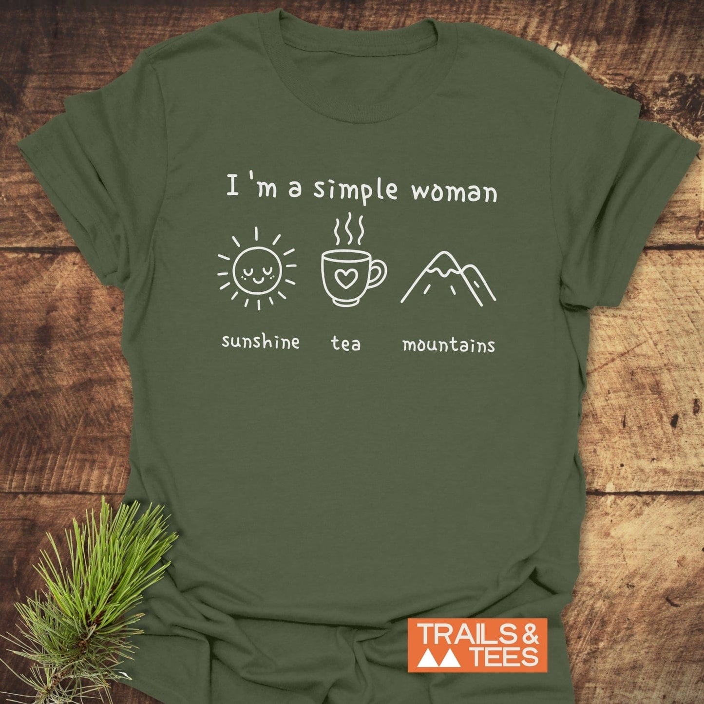 I'm A Simple Woman - Sunshine Tea Mountains T-Shirt features white hand-drawn icons of a sun, mug, and peaks on a forest-green fabric, with TRAILS & TEES logo.