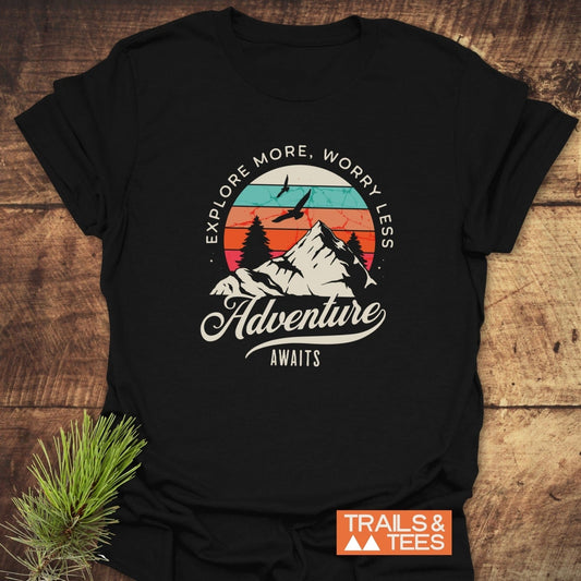 Adventure Awaits Retro T-Shirt featuring a vintage outdoor graphic with a sunset, mountains, and trees. Made from soft cotton, ideal for outdoor enthusiasts.