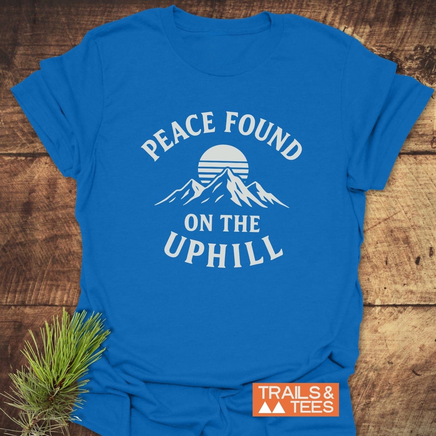 Peace Found T-Shirt featuring a stylized mountain graphic with “PEACE FOUND ON THE UPHILL” slogan and Trails & Tees logo, emphasizing an outdoorsy theme.