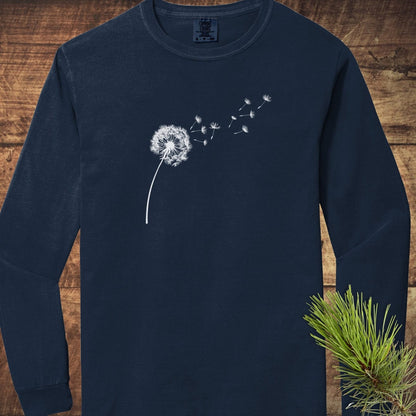 Dandelion Comfort Colors Long-Sleeve Tee in navy, featuring a white dandelion print, laid flat with a pine sprig accent, showcasing its soft, relaxed fit.