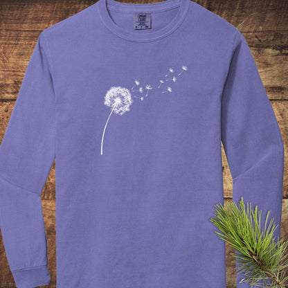 Dandelion Comfort Colors Long-Sleeve Tee: lavender-purple, 100% ring-spun cotton, relaxed fit, featuring a white dandelion silhouette on front, laid on wooden background.