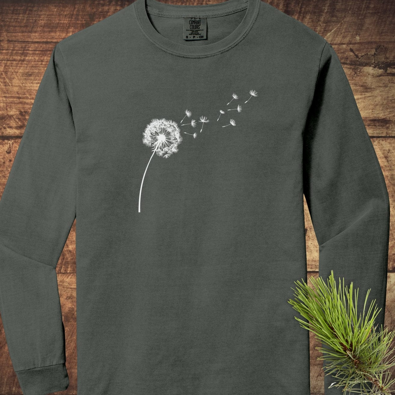 Dandelion Comfort Colors Long-Sleeve Tee featuring a white dandelion design, laid flat with pine sprig accent. Made of soft, 100% ring-spun cotton.