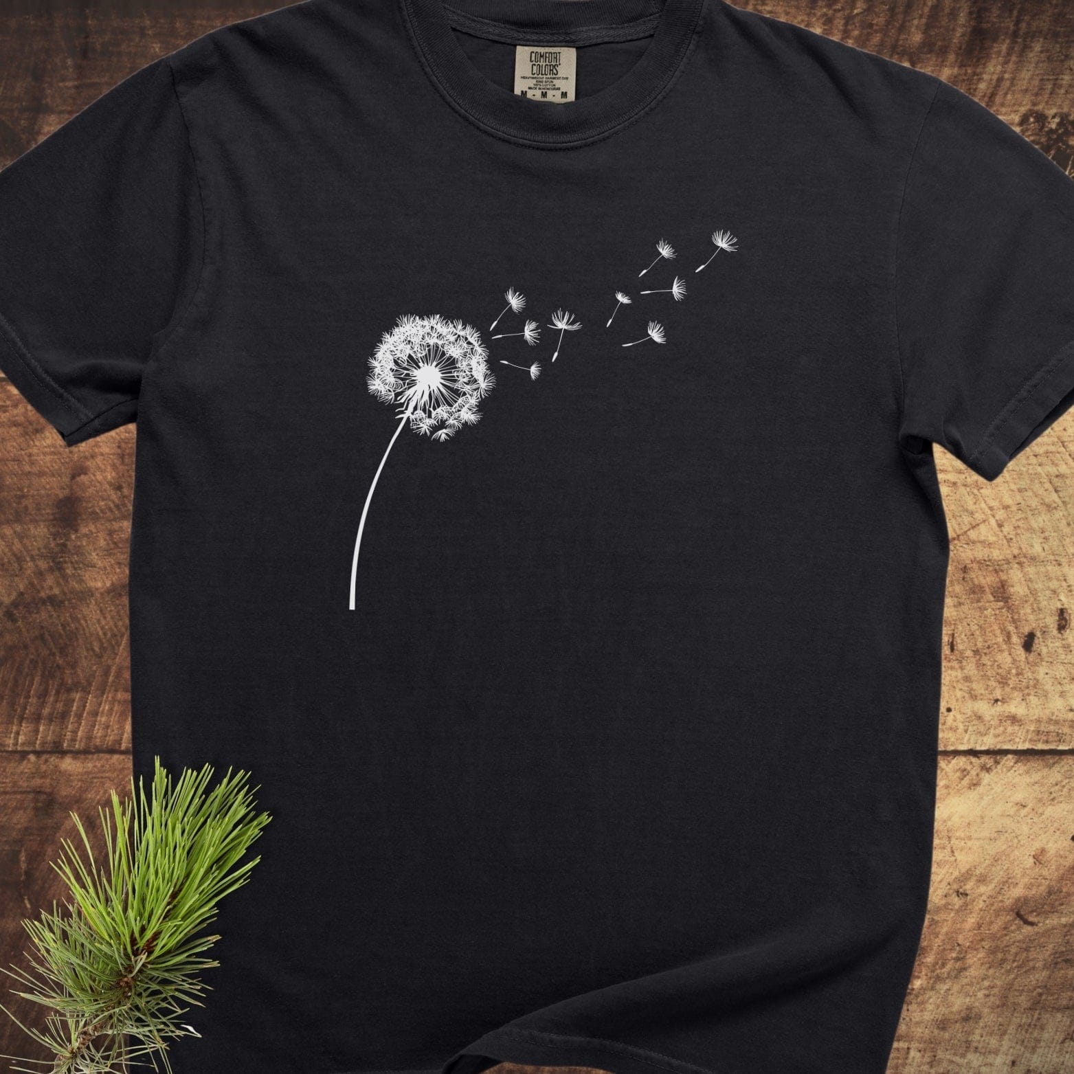 Dandelion Comfort Colors 1717 Tee with a white dandelion print on black fabric, laid flat, showcasing short sleeves and a Comfort Colors label.