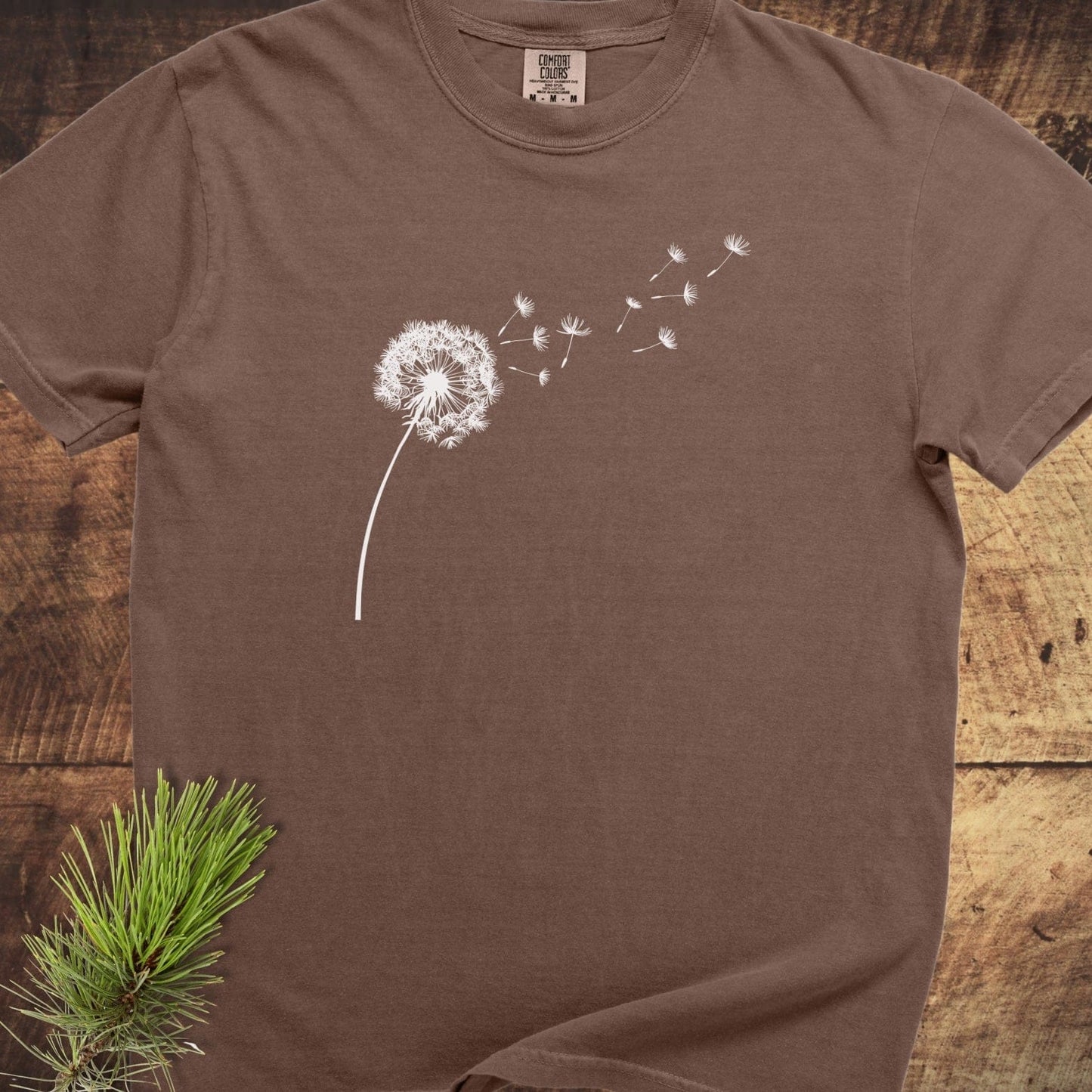 Dandelion Comfort Colors 1717 Tee: Earth-tone tee with white dandelion graphic, laid flat, showcasing its relaxed fit and soft-washed, garment-dyed cotton texture.