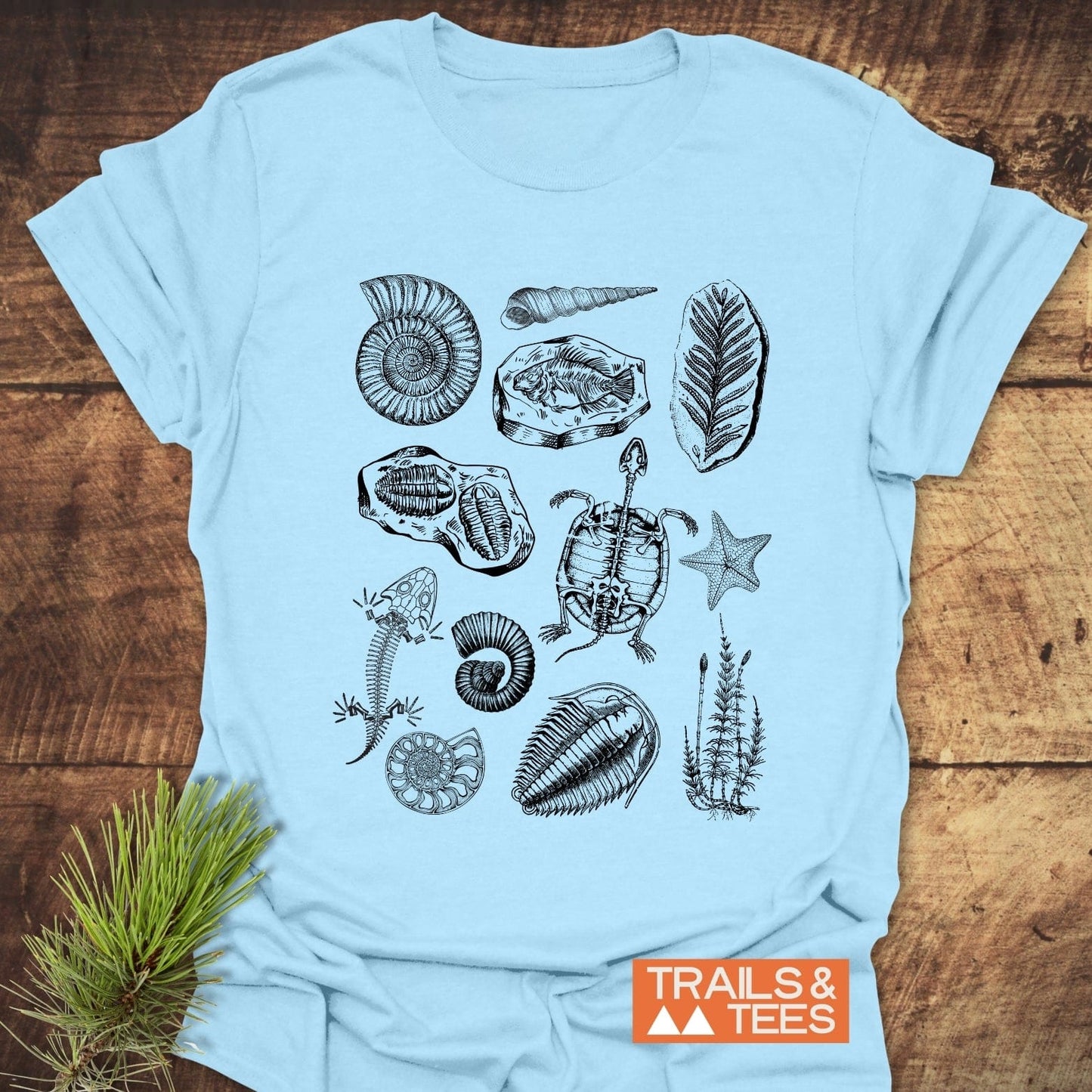 Fossile Vintage Tattoo T-Shirt featuring hand-drawn fossil and skeleton motifs, including ammonite, trilobites, and a fish, with Trails & Tees logo.
