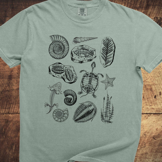 Fossile Vintage Tattoo Comfort Colors 1717 Tee featuring black fossil and skeleton illustrations, including ammonites and trilobites, on a pale-green, relaxed-fit, 100% cotton shirt.