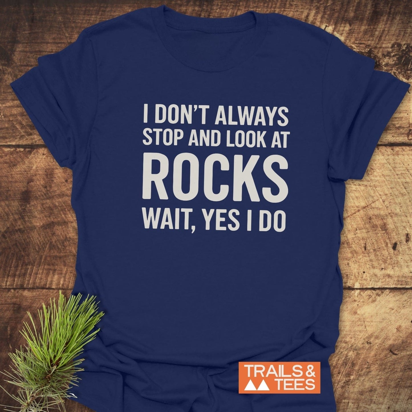 Navy-blue I Don't Always... Rock Lover T-Shirt with bold white text, TRAILS & TEES logo, and pine sprig on rustic wood background.