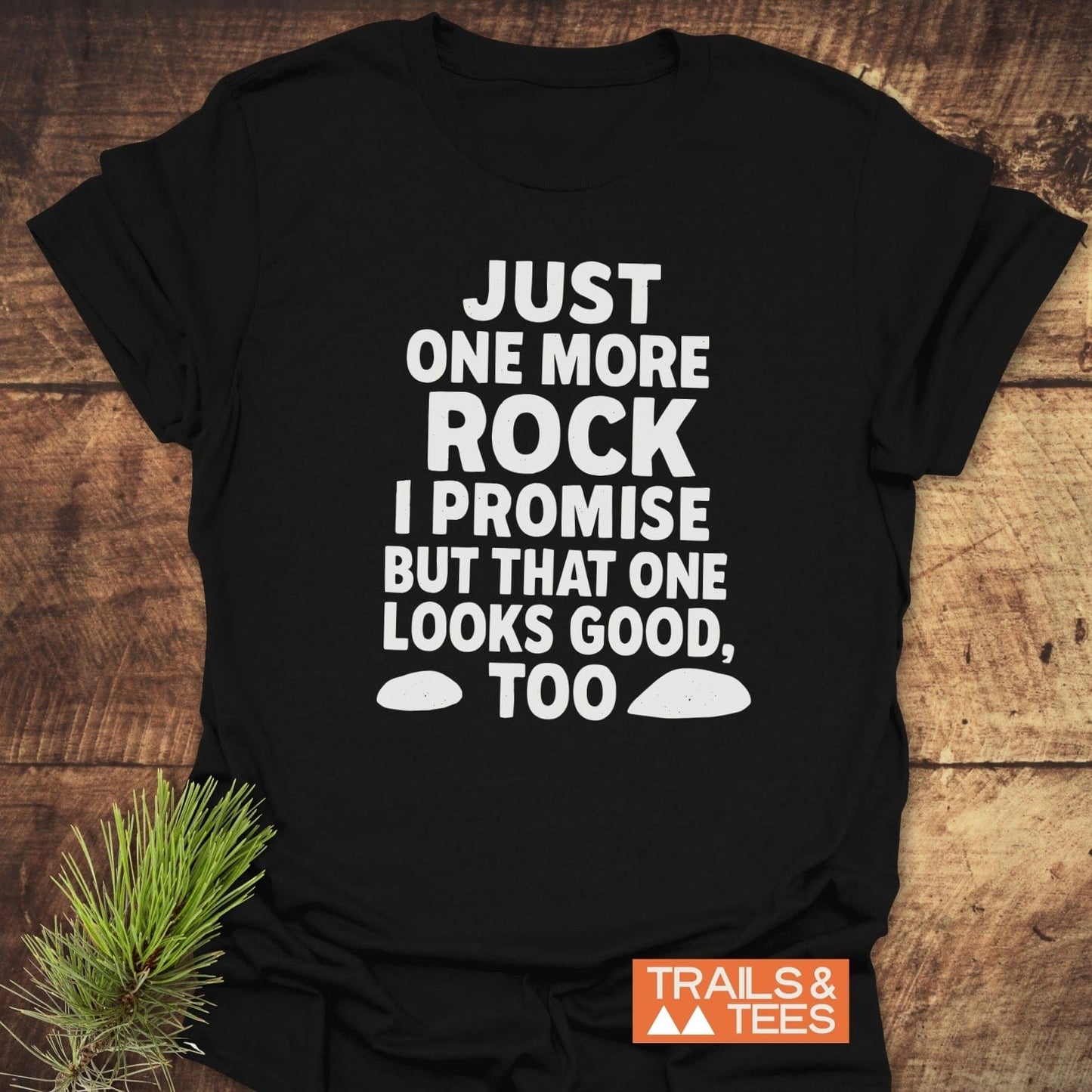 Black T-shirt with bold white slogan: JUST ONE MORE ROCK I PROMISE BUT THAT ONE LOOKS GOOD, TOO, featuring Trails & Tees logo.