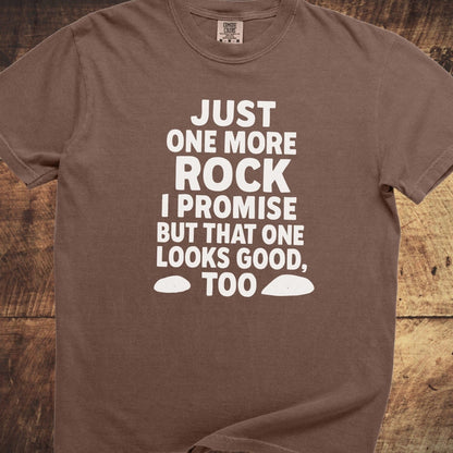 Just One More Rock Funny Comfort Colors 1717 Tee with humorous white text and rock shapes, laid on a wooden surface, showcasing its relaxed fit and durable stitching.