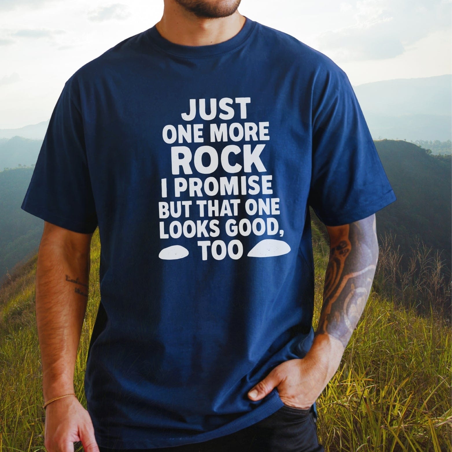 Person wearing Just One More Rock navy Comfort Colors 1717 Tee, featuring white text and rock graphics, standing outdoors with visible bracelet and tattoo.