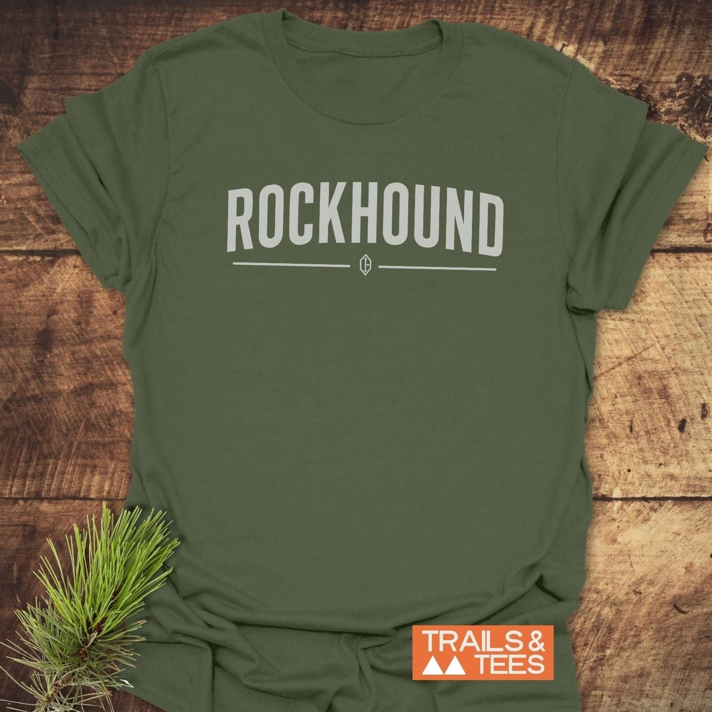 Olive-green Rockhound Rock Lovers T-Shirt with ROCKHOUND text, gem icon, and TRAILS & TEES logo, accented by a pine needle sprig.