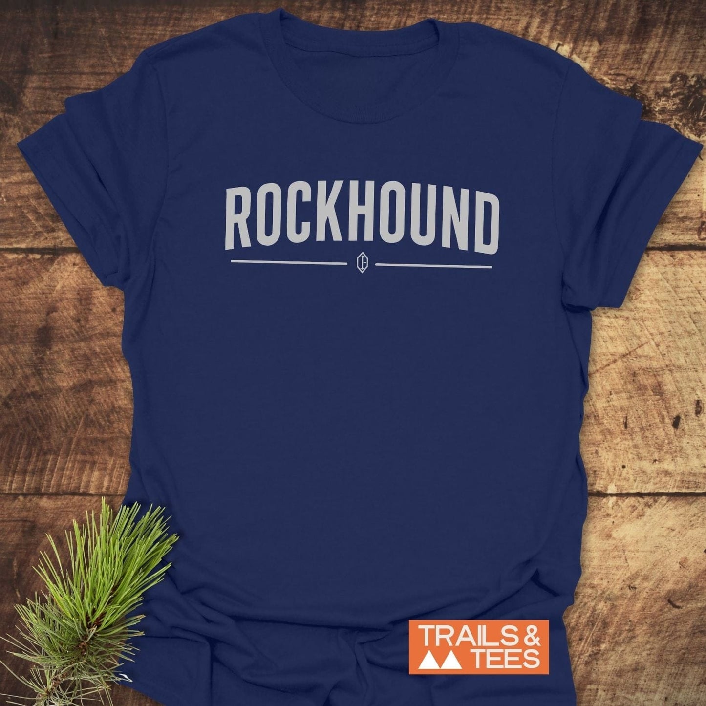 Rockhound Rock Lovers T-Shirt featuring bold ROCKHOUND text and emblem, displayed on a wooden surface with a TRAILS & TEES label.