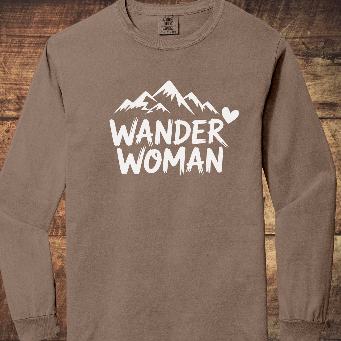 Wander Woman Comfort Colors Long-Sleeve Tee featuring a stylized mountain graphic and text, laid flat, showcasing its soft, garment-dyed 100% ring-spun cotton fabric.