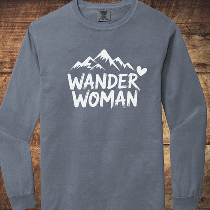 Wander Woman Comfort Colors Long-Sleeve Tee with a stylized mountain and heart design, offering softness and a relaxed fit, laid flat on wood.