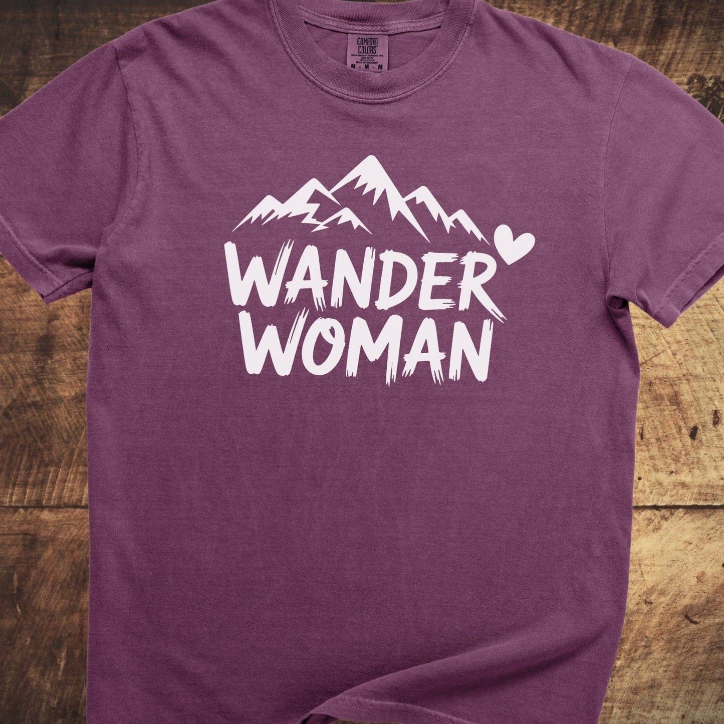 Wander Woman Comfort Colors 1717 Tee featuring a white mountain graphic and text on a plum-colored shirt, showcasing a relaxed fit and soft-washed cotton.