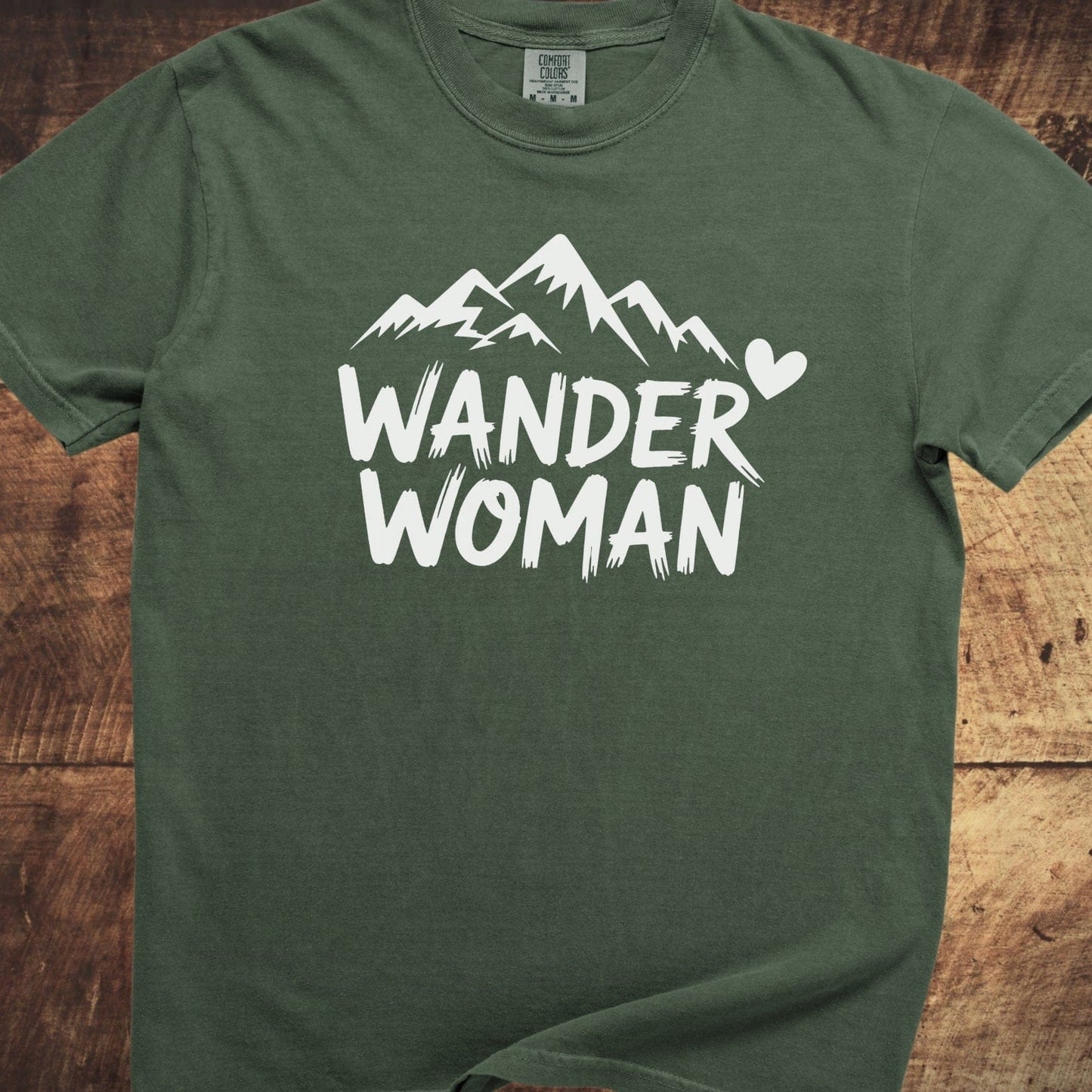 Wander Woman Comfort Colors 1717 Tee with a mountain graphic and text on an olive-green short-sleeve, laid flat, showcasing its relaxed fit and durable stitching.