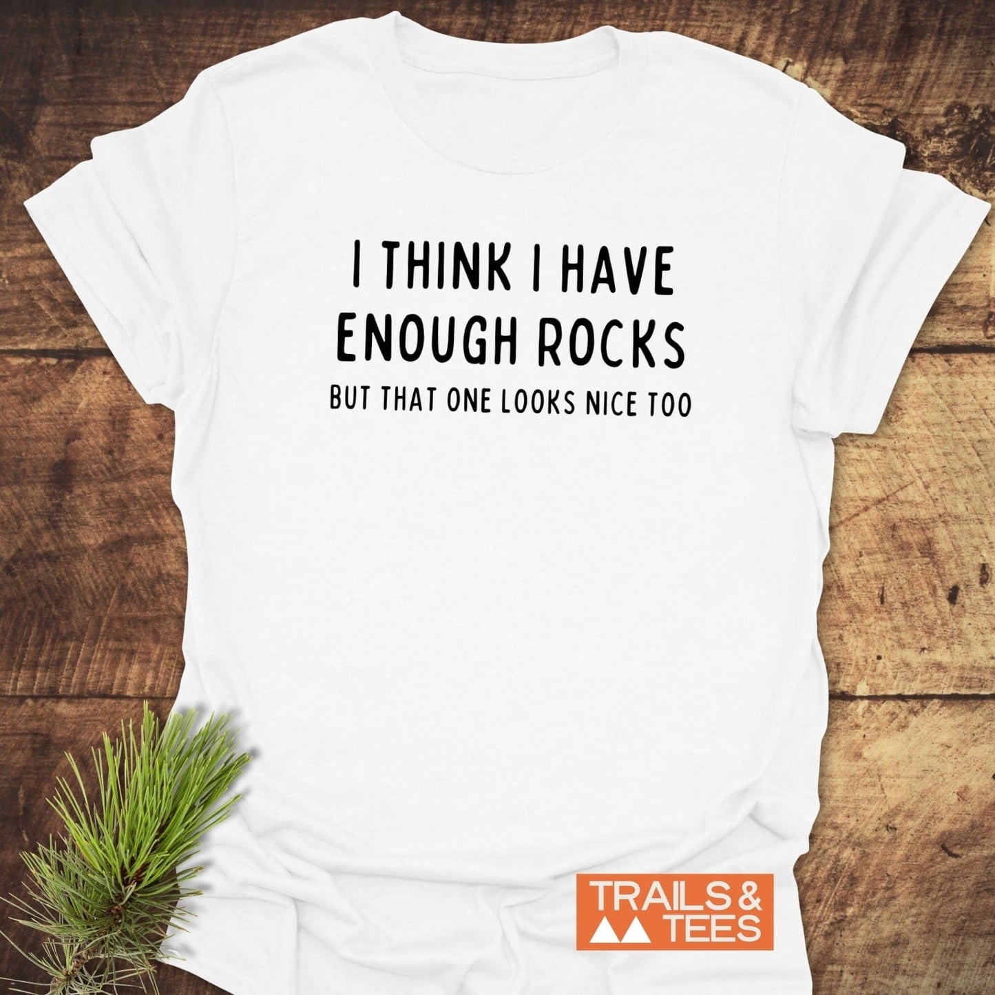 Enough Rocks T-Shirt featuring playful text, laid flat with pine sprig. Made from soft ring-spun cotton, it offers comfort for outdoor enthusiasts.