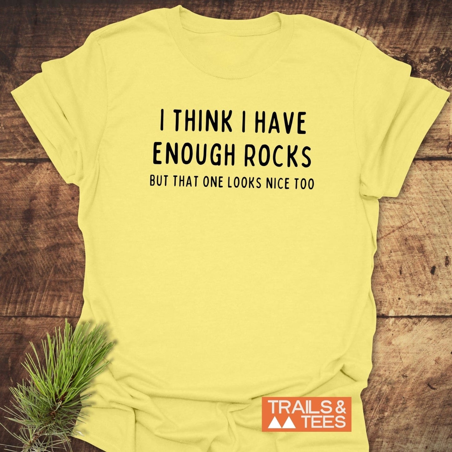 Enough Rocks T-Shirt featuring witty text, small TRAILS & TEES logo, styled with pine needles, highlighting comfort and durability for outdoor enthusiasts.