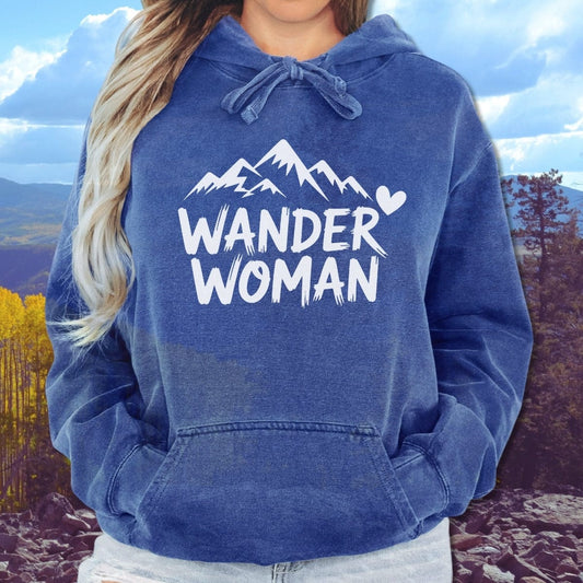 Person wearing Wander Woman Comfort Colors Hoodie with mountain graphic, hands in pocket, showcasing relaxed fit and cozy fleece material ideal for outdoor adventures.