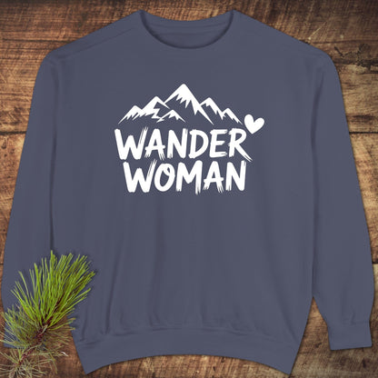 Navy Wander Woman sweatshirt featuring white mountain peaks and heart graphic, laid flat on wood with evergreen sprig, showcasing relaxed fit and premium fabric.