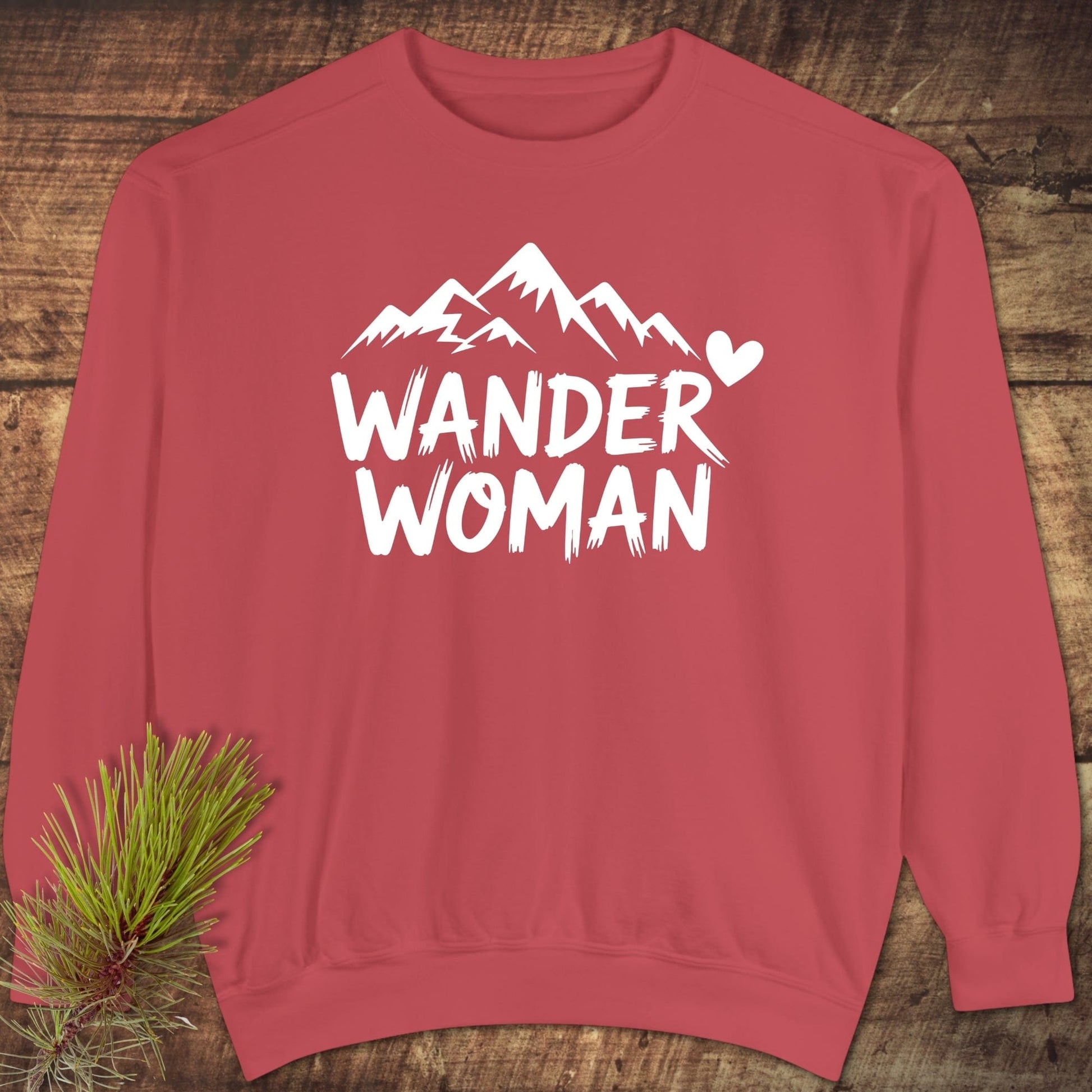 Wander Woman Sweatshirt with a white mountain design and heart, laid on wood. Features relaxed fit, ring-spun cotton blend, and garment-dyed fleece.