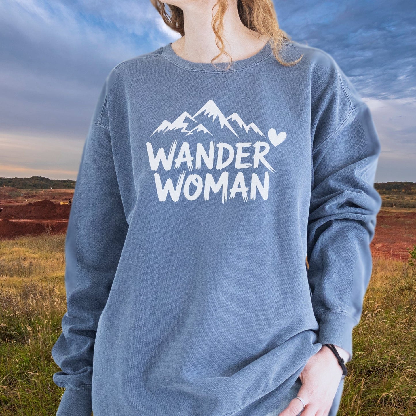 Woman outdoors wearing a slate-blue Wander Woman Sweatshirt with mountain graphic, showcasing its relaxed fit and luxurious, garment-dyed fabric.
