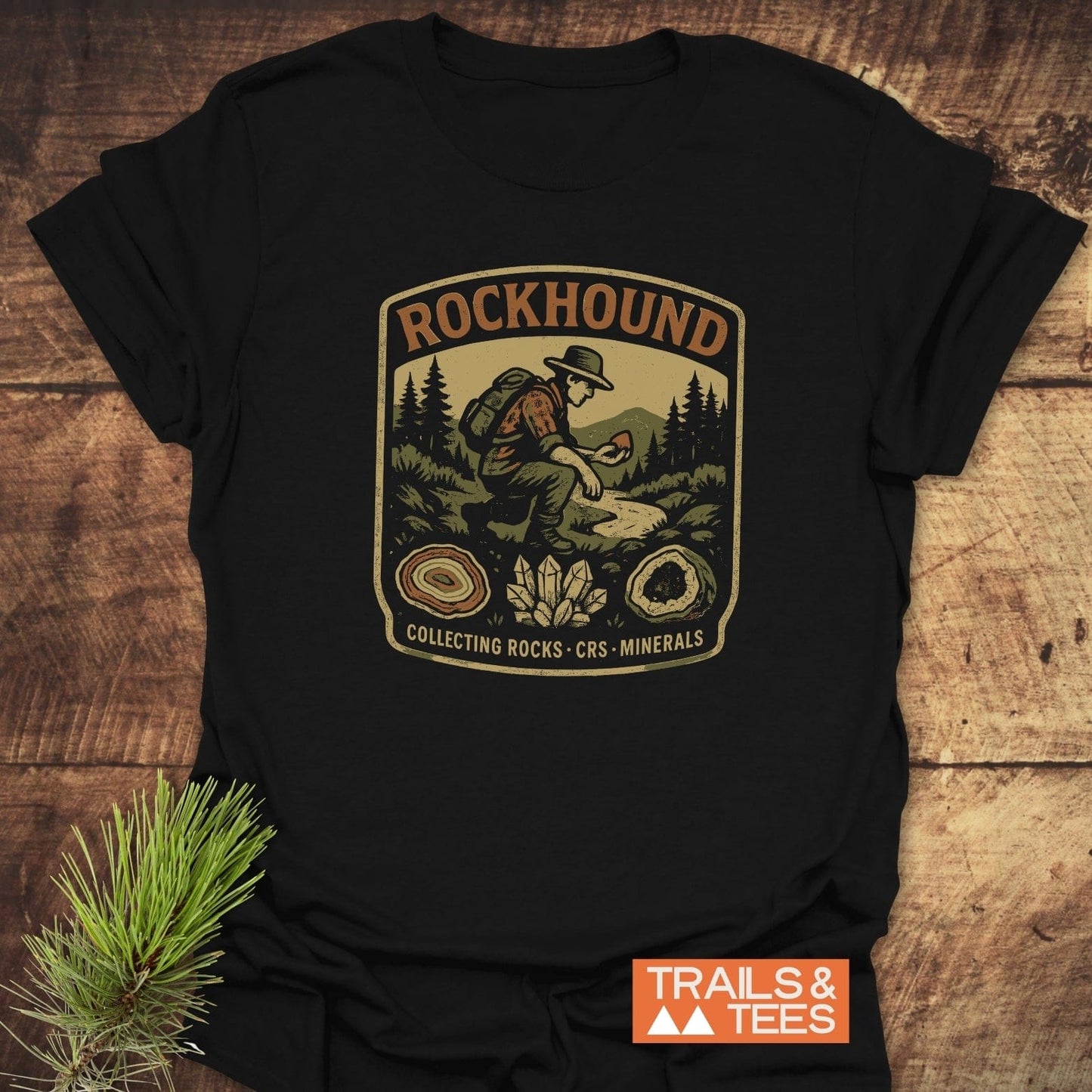 Rockhound Badge T-Shirt featuring vintage patch artwork of a hiker in mountains with geodes and crystals, showcasing outdoor adventure spirit and durable design.