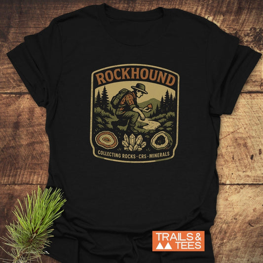Rockhound Badge T-Shirt featuring vintage patch artwork of a hiker in mountains with geodes and crystals, showcasing outdoor adventure spirit and durable design.