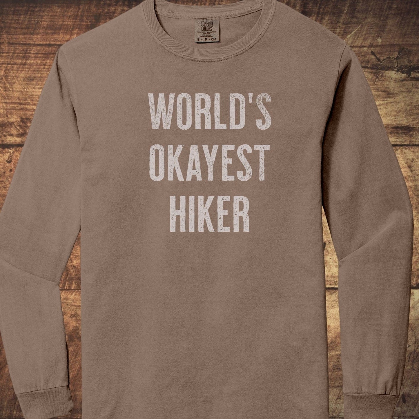 World's Okayest Hiker Comfort Colors Long-Sleeve Tee, featuring white text on brown, made of 100% ring-spun cotton with a relaxed fit for comfort.