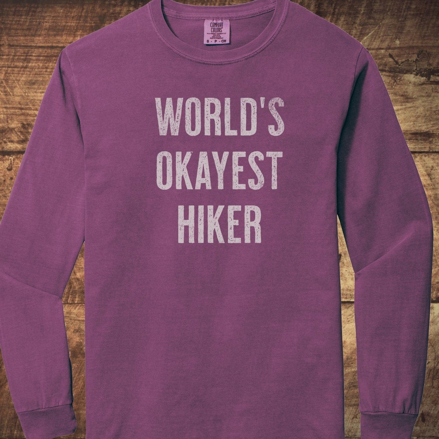 World's Okayest Hiker Comfort Colors Long-Sleeve Tee with distressed white lettering, crewneck design, showcasing a relaxed fit in soft, 100% ring-spun cotton.