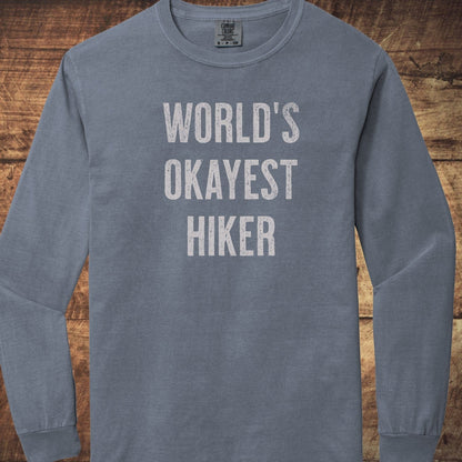 World's Okayest Hiker Comfort Colors Long-Sleeve Tee featuring slate-blue fabric, distressed white lettering, and a classic crewneck design for a relaxed fit.