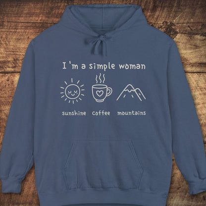 I'm A Simple Woman Comfort Colors Hoodie featuring sunshine, coffee, mountains icons, front kangaroo pocket, drawstring hood, and relaxed fit, laid on wooden background.