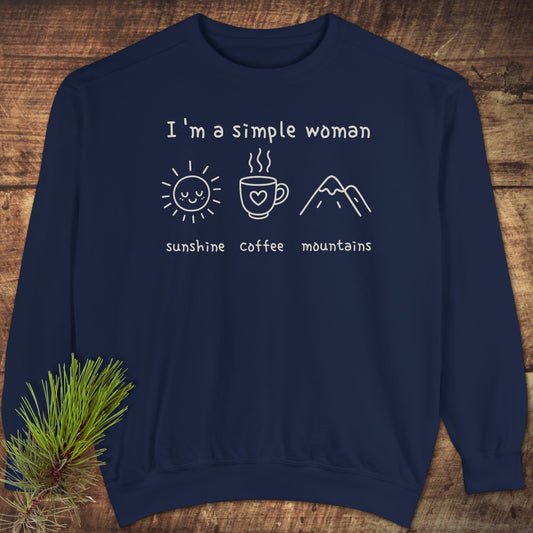 I'm A Simple Woman Comfort Colors 1566 Sweatshirt featuring sunshine, coffee, mountains icons on navy-blue, displayed on wood with a pine sprig.