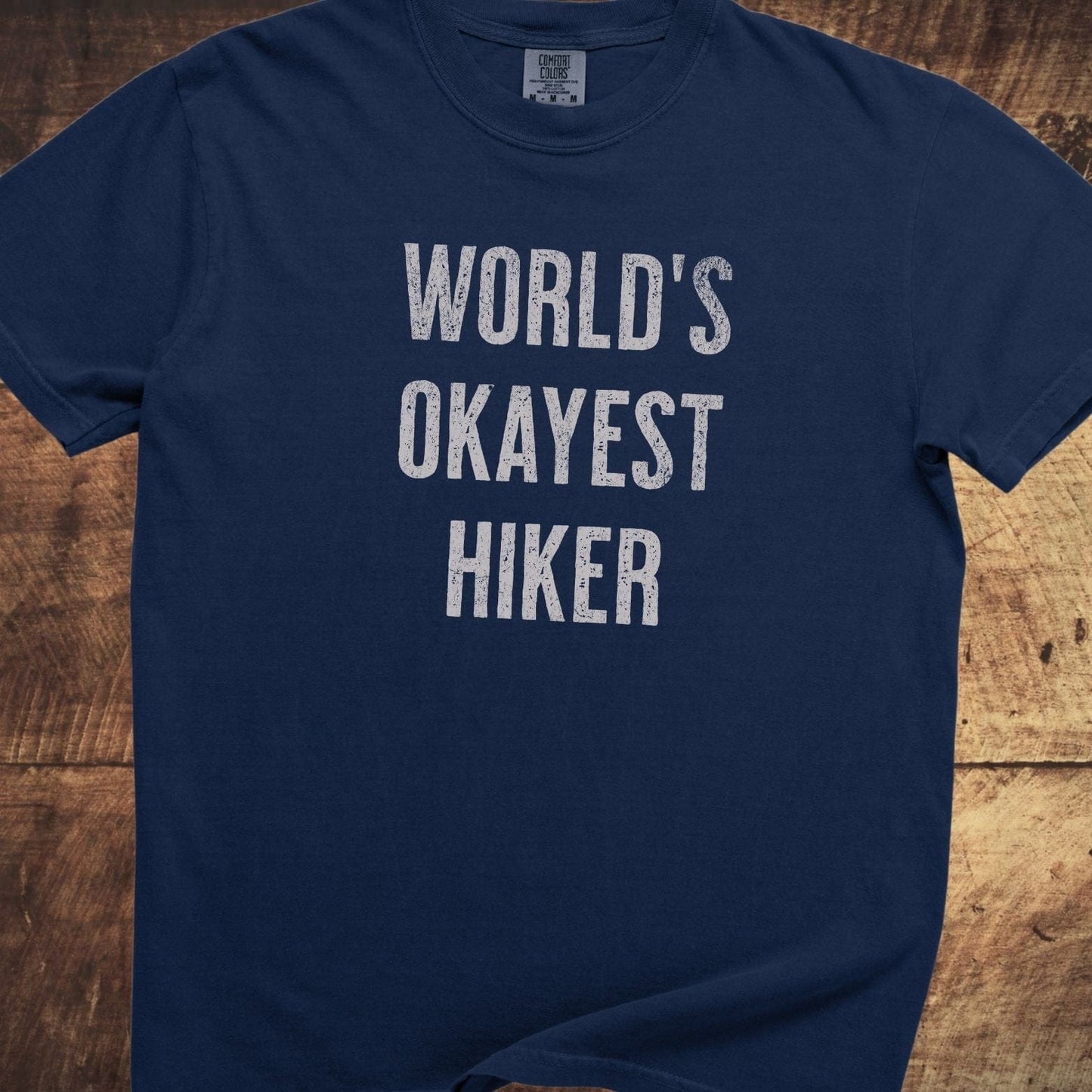World's Okayest Hiker Comfort Colors 1717 Tee in navy, laid flat, featuring distressed white lettering. Made of soft, 100% ring-spun cotton for a relaxed fit.