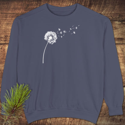 Dandelion Comfort Colors Sweatshirt in slate blue with a white dandelion graphic, displayed on wood. Features a relaxed fit, ring-spun cotton blend, and garment-dyed fabric.